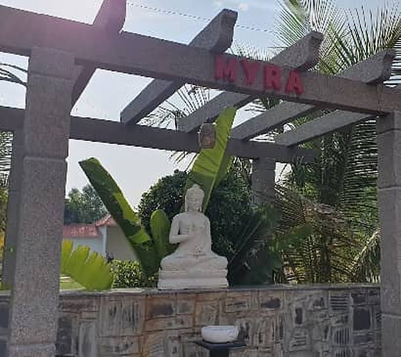 Stone pergola with the Myra name and a white Buddha statue in the garden